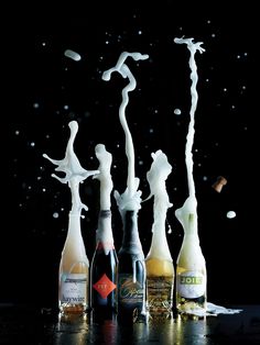 four bottles with white liquid pouring out of them on a black surface, in the shape of figures