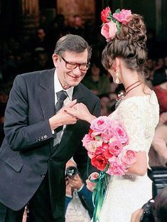 a man and woman standing next to each other in front of a crowd holding flowers