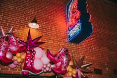 balloon decorations on the side of a brick building with a neon sign in the background