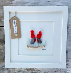 two birds sitting on top of a branch in a white frame with a tag hanging from it