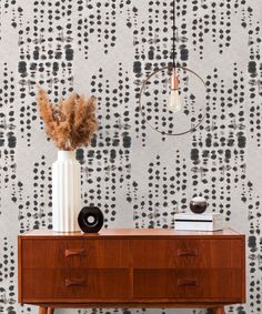 a wooden dresser with a white vase on top of it next to a wallpaper