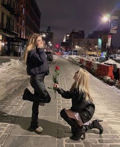 two women kneeling down on the sidewalk and one is holding a rose in her hand