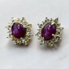 A stunning, richly colored set of untreated and unheated, natural Star Rubies. The larger of the two gems originates from Burma, the other, India; but they are well matched in color. These have been set in prefabricated yellow gold plated, sterling silver settings with white Topaz accents. These are bold and beautiful with a sophisticated feeling to the design and will certainly dazzle! Dazzling Ruby Gemstone Earrings, Luxury Gemstone Cluster Earrings For Anniversary, Luxury Gemstone Cluster Earrings, Luxury Round Gemstone Cluster Earrings, White Topaz Earrings, Star Ruby, Topaz Earrings, Sterling Silver Studs, White Topaz