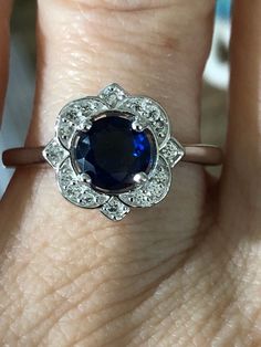 We loved this original vintage natural 1.3CT round cut royal blue sapphire ring with a floral halo of white sapphires. The original ring was from the 1990s in Norway. It was in perfect condition and sold quickly, so we replicated it exactly for you but in a more affordable version with all the beauty of the original. Ring Box created blue sapphire natural white topaz halo 925 sterling silver 14K white gold Classic Royal Blue Round Sapphire Ring, Elegant Blue Diamond Flower Ring, Royal Blue Sapphire Ring Fine Jewelry, Vintage Gia Certified Sapphire Ring Gift, Vintage Gia Certified Sapphire Ring, Vintage Blue Sapphire Ring With Halo Setting, Vintage Sapphire Ring With Halo Setting, Vintage Blue Cluster Ring With Prong Setting, Blue Sapphire Heirloom Ring With Halo Design