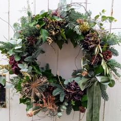 a wreath is hanging on the side of a door with greenery and pine cones