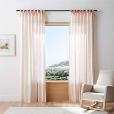 a white rocking chair in front of a window with pink drapes on the windowsill