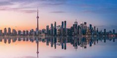 the skyline of toronto is reflected in the water at sunset, with skyscrapers and other high rise buildings behind it