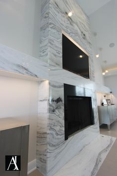 a large white marble fireplace in the middle of a room with two televisions on it's sides