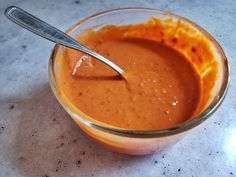 a glass bowl filled with sauce on top of a counter next to a metal spoon