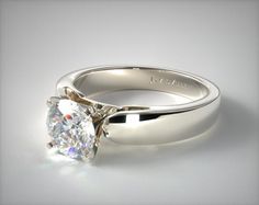 a white gold engagement ring with a round brilliant cut diamond in the center, on a plain surface