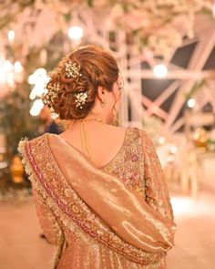 the back of a woman's head with flowers in her hair, wearing a gold dress