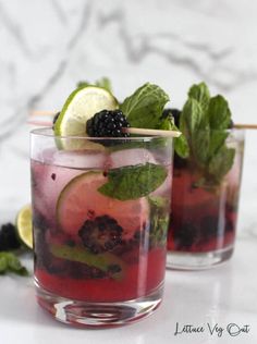 two glasses filled with blackberry mojita on top of a table