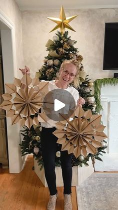 a woman standing in front of a christmas tree holding two large paper fan shaped decorations