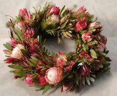 a wreath with pink flowers and greenery on it sitting on a white sheeted surface