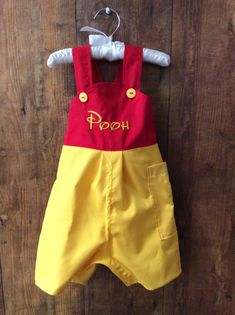 a yellow and red romper with the word pooh on it hanging from a hook