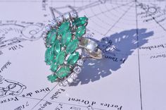 The Aldridge Vintage Emerald & Diamond Modified Navette Cluster Ring. The ring is set with 5.60 carats of natural emeralds in marquise shape and on either side of the center section is 0.60 carats total weight by measurement of diamonds. This ring tested as 14 karat white gold.This ring is currently a size 8, but can be adjusted to any finger size. Each piece has been hand selected and meticulously identified and graded by a Graduate Gemologist who has been awarded a degree by the Gemologica Fine Jewelry Marquise Emerald Ring With 17 Jewels, Marquise Emerald Ring For Formal Occasions, Filigree Engagement Ring, Antique Diamond Rings, About Page, Filigree Ring, Antique Diamond, Emerald Diamond, Natural Emerald