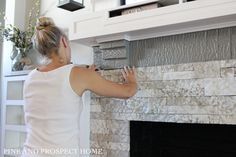 a woman is painting a stone fireplace with white paint and silver foil on the mantle