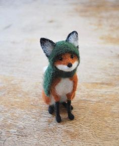 a small toy fox wearing a green hat and scarf on top of a wooden floor