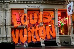 an orange sign that says louis vuitton in front of a building with graffiti on it