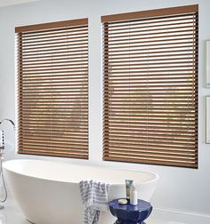 a white bath tub sitting next to two windows with wooden blinds on them in a bathroom