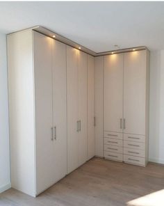 an empty room with white cupboards and lights on the wall, in front of a wooden floor