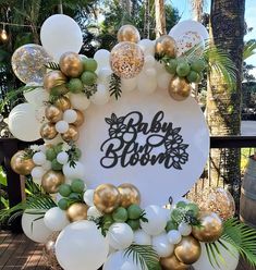 a baby shower sign surrounded by balloons and greenery in front of a palm tree