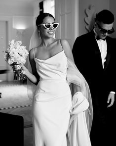 a woman in a white dress is walking with a man wearing a tuxedo