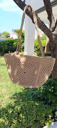 a handbag hanging from a tree in front of a house with grass and bushes