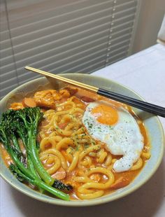 a bowl filled with noodles, broccoli and an egg