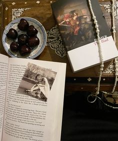 an open book sitting on top of a table next to a plate of fruit and beads