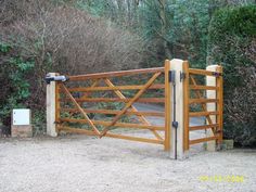 a wooden gate in the middle of a dirt area with trees and bushes behind it