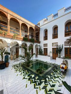 an outdoor courtyard with potted plants and decorative tiles on the floor, in front of a large white building