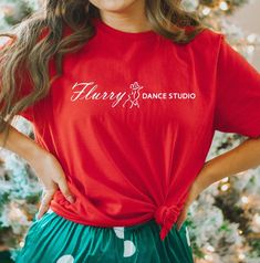 a woman standing in front of a christmas tree wearing a red shirt with the words harry dance studio on it