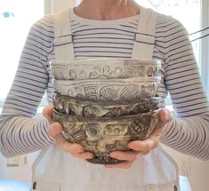 a woman is holding three bowls in her hands while wearing an apron and striped shirt