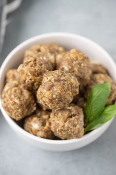 a white bowl filled with meatballs next to a green leaf on top of a table