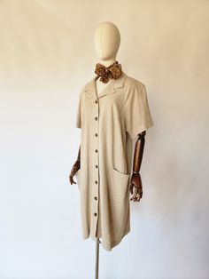 Vintage shirt dress is quintessential 1980's. It is made of a khaki linen fabric and is very comfrontable. The dress features a v-neckline, a chic neckscarf, short sleeves, side hip pockets, a hemline that falls below the knee, and tortise brown colored button down closures at the front. A great work dress and addition to any wardrobe. size: best fits, US medium bust - 46 inches waist -47 inches sleeves - 15 inches hips - 48 inches length - 41 inches scarf: 41 inches long material - linen, butto Collared Beige Cotton Shirt Dress, Collared Beige Linen Shirt Dress, Beige Collared Linen Shirt Dress, Beige Linen Collared Shirt Dress, Beige Linen Shirt Dress With Button Closure, Oversized Vintage Summer Dress, Vintage Shirt Dress, Linen Shirt Dress, Dress Xl