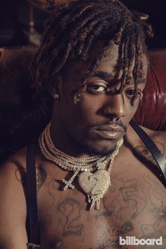 a man with tattoos on his chest sitting in a leather chair and wearing a chain around his neck