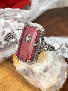 This is a lovely antique Edwardian era inspired filigree ring. This gorgeous ring is created in stunning rose-pink camphor glass. This gorgeous ring is set with a stunning carved floral pink glass/resin with a centered set 1mm white gem. Please choose between white Cubic Zirconia (CZ), lab created Moissanite or a natural Diamond. The camphor glass is 18mm x 9mm. The ring sits 21mm north-south and 12mm east-west on the finger. The inside of the band is marked 925 for solid sterling silver. Victorian Filigree Ring With Cabochon For Gift, Vintage Pink Jewelry For Anniversary, Pink Vintage Jewelry For Anniversary, Antique Pink Jewelry With Rose Cut Diamonds, Antique Pink Rose Cut Diamond Jewelry, Victorian Pink Rose Cut Diamond Jewelry, Vintage Pink Cabochon Ring, Antique Filigree Cabochon Ring Gift, Antique Filigree Ring With Cabochon For Gift