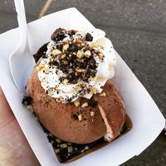 a hand holding a pastry with whipped cream and toppings on top in a paper container