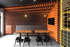 an orange and black room with chairs, tables and large pipes on the wall behind it