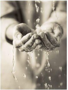 a person is holding their hands under water from a faucet in black and white