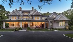 a large house with lots of windows and lights on it's front porch, surrounded by lush green trees