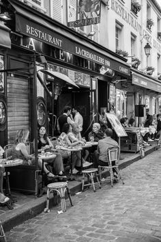 black and white photograph of people sitting at outdoor tables in front of an italian restaurant