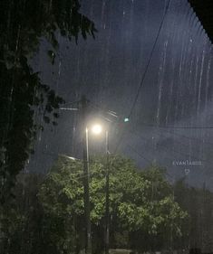 the street light is lit up on a rainy night with rain coming down in the background