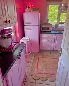 a pink kitchen with an old fashioned refrigerator and stove top oven, rug on the floor