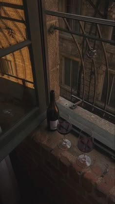 two wine glasses sitting on top of a window sill next to a beer bottle