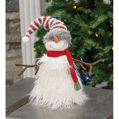 a snowman with a red and white hat is sitting in front of a christmas tree