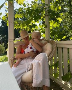 a woman sitting in a wicker chair with a baby on her lap while holding the child