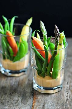 two small glass cups filled with food on top of a wooden table next to each other