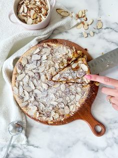 a person cutting into a cake on top of a wooden board next to a bowl of nuts